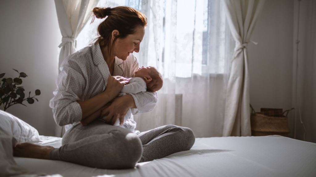 mother holding neworn baby and sitting on bed: placenta helps you heal postpartum